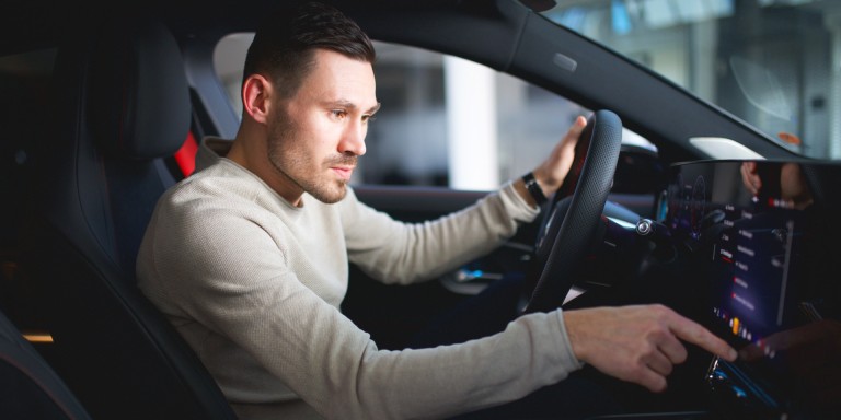 
				Felix B�llmann, Customer Onboarding f�r Digitale Extras bei Mercedes-Benz, sitzt auf dem Fahrersitz eines Mercedes-Benz CLA und bedient mit der rechten Hand den Zentralbildschirm.
				