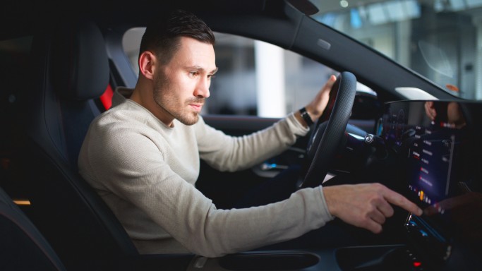 
				Felix B�llmann, Customer Onboarding f�r Digitale Extras bei Mercedes-Benz, sitzt auf dem Fahrersitz eines Mercedes-Benz CLA und bedient mit der rechten Hand den Zentralbildschirm.
				