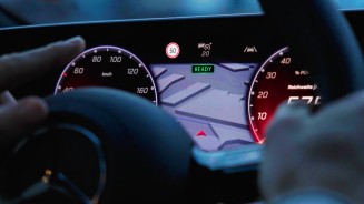 
Nahaufnahme des Fahrerbildschirms eines Mercedes-Benz Fahrzeugs. Ein Zeigefinger deutet auf die Geschwindigkeitsanzeige, die der Verkehrszeichenassistent in Form eines Icons eines 50-kmh-Schilds auf dem Fahrerbildschirm einblendet.
