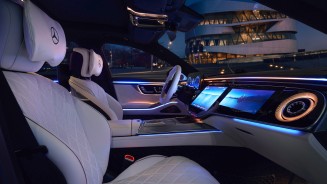 
as Bild zeigt den Innenraum der neuen S-Klasse mit AMG Line Interieur und Exklusiv-Paket in MANUFAKTUR tiefwei� / schwarz aus der Perspektive der ge�ffneten Beifahrert�r. Sichtbar sind die wei�en Ledersitze mit gestepptem Muster und integrierten Kopfst�tzen, das Multifunktionslenkrad sowie der MBUX Superscreen mit digitalen Displays �ber die gesamte Instrumententafel. Die Ambientebeleuchtung in Blau und Warmt�nen verl�uft entlang der T�ren und des Armaturenbretts. Durch die Seitenscheibe ist im Hintergrund das beleuchtete Mercedes-Benz Museum bei Nacht zu sehen.
