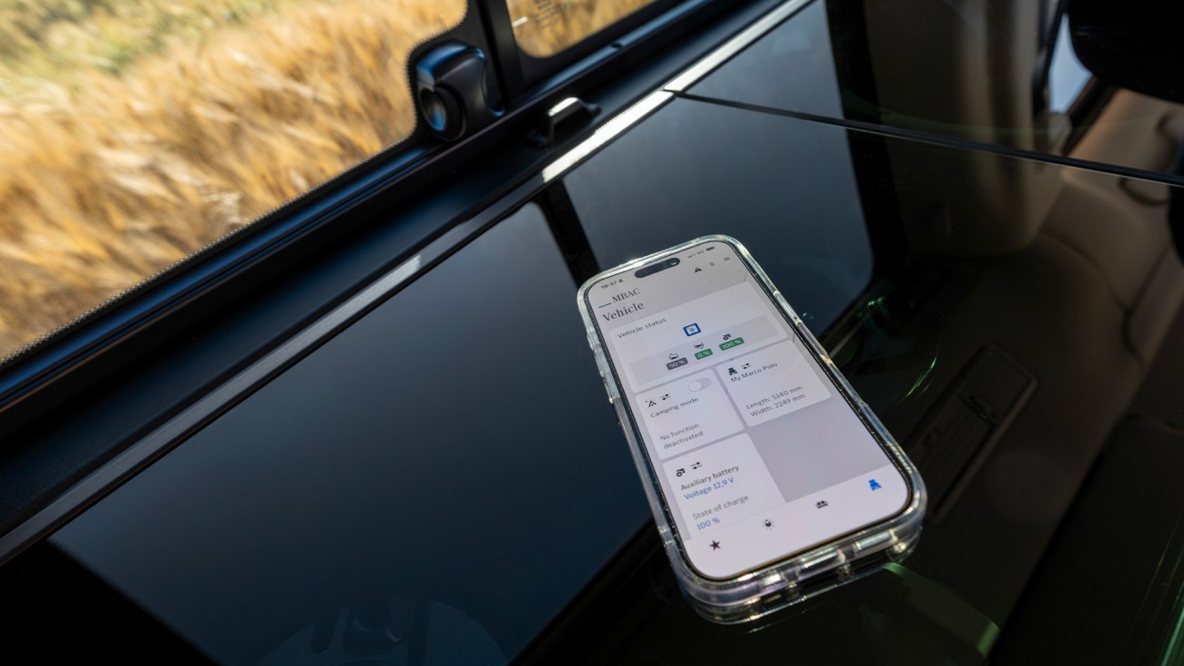 
			Ein Smartphone liegt auf der K�chenzeile eines Mercedes-Benz Marco Polo. Auf dem Display sind grob die Fahrzeugfunktionen erkennbar, die �ber das Smartphone gesteuert werden k�nnen. Durch das Seitenfenster, das oberhalb des Smartphones erkennbar ist, ist eine Graslandschaft zu erkennen.
		