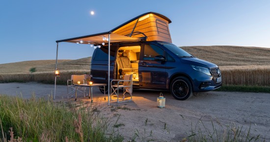 
					  Seitliche Ansicht des neuen Mercedes-Benz Marco Polo in der Farbe sodalithblau metallic, der bei einsetzender D�mmerung in einer weitl�ufigen Landschaft steht. Das Aufstelldach ist ge�ffnet, die Markise ausgefahren und der beleuchtete Innenraum durch die ge�ffnete Schiebet�r sichtbar. Unter der Markise stehen ein Tisch und zwei Campingst�hle. Im Hintergrund erstrecken sich Felder und sanfte H�gel unter blauem Himmel.
					  