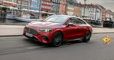 
					  Der elektrische CLA in MANUFAKTUR patagonienrot metallic f�hrt auf einer Uferstra�e entlang. Das Fahrzeug ist schr�g von vorn zu sehen. Im Hintergrund sind ein Kanal mit mehreren Booten sowie farbenfrohe H�userfassaden erkennbar. Rechts unten im Bild ist das Logo &bdquo;Car of the Year&ldquo; aus dem Jahr 2026 platziert.
					  