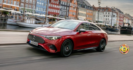 
					  Der elektrische CLA in MANUFAKTUR patagonienrot metallic f�hrt auf einer Uferstra�e entlang. Das Fahrzeug ist schr�g von vorn zu sehen. Im Hintergrund sind ein Kanal mit mehreren Booten sowie farbenfrohe H�userfassaden erkennbar. Rechts unten im Bild ist das Logo &bdquo;Car of the Year&ldquo; aus dem Jahr 2026 platziert.
					  