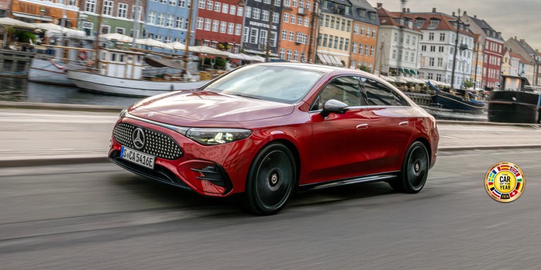 
				Der elektrische CLA in MANUFAKTUR patagonienrot metallic f�hrt auf einer Uferstra�e entlang. Das Fahrzeug ist schr�g von vorn zu sehen. Im Hintergrund sind ein Kanal mit mehreren Booten sowie farbenfrohe H�userfassaden erkennbar. Rechts unten im Bild ist das Logo &bdquo;Car of the Year&ldquo; aus dem Jahr 2026 platziert.
				