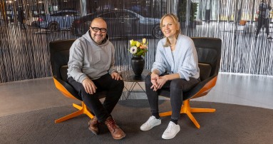 
					  Frank Kemmerer sitzt links neben Veronika Kl�nder in einem modernen Sitzbereich im Mercedes-Benz Kundencenter Sindelfingen. Zwischen ihnen steht ein kleiner runder Tisch, darauf eine Vase mit Blumenstrau� in gelb, orange und wei�. Beide l�cheln sitzend, leicht nach vorne gebeugt in die Kamera. Frank tr�gt einen hellgrauen Kapuzenpullover mit Mercedes-Stern, eine dunkle Hose und braune Schuhe. Veronika tr�gt eine hellblaue Strickjacke, schwarze Jeans und wei�e Sneaker. Im Hintergrund ist dunkler Fadenvorhang zu sehen. Hinter dem Vorhang erkennt man schemenhaft Ausstellungsfahrzeuge.
					  