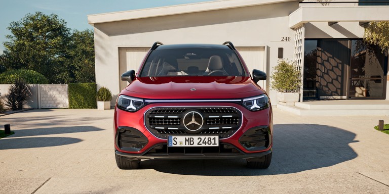 
				Der neue GLB mit Hybrid-Technologie in MANUFAKTUR patagonienrot metallic steht vor einer beigefarbenen Garage in einer Einfahrt. Das Fahrzeug ist frontal zu sehen. Im Hintergrund sind B�ume und ein Hauseingang.
				