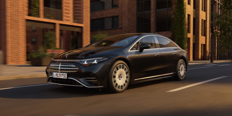 
				Ein Mercedes-Benz EQS in MANUFAKTUR schwarz sparkling f�hrt in der Abendsonne auf einer Stra�e an einem Backsteingeb�ude mit gro�er Fensterfront vorbei.
				