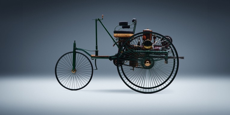 
				In einem leeren Raum steht in der Mitte beleuchtet das erste Automobil von Mercedes-Benz.
				