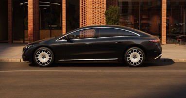 
					  Ein Mercedes-Benz EQS Limousine in MANUFAKTUR black sparkling steht auf einem Parkplatz vor dem Eingang eines Backsteingeb�udes mit gro�z�gigen Fensterscheiben. 
					  