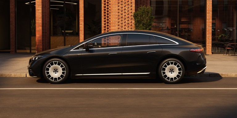 
				Ein Mercedes-Benz EQS Limousine in MANUFAKTUR black sparkling steht auf einem Parkplatz vor dem Eingang eines Backsteingeb�udes mit gro�z�gigen Fensterscheiben. 
				