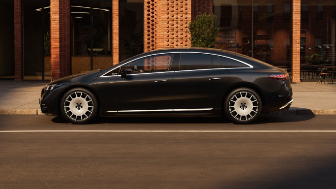 
				Ein Mercedes-Benz EQS Limousine in MANUFAKTUR black sparkling steht auf einem Parkplatz vor dem Eingang eines Backsteingeb�udes mit gro�z�gigen Fensterscheiben. 
				