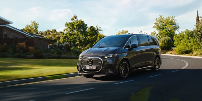 
				Der Mercedes-Benz VLE in obsidianschwarz metallic f�hrt auf einer leicht geschwungenen Stra�e an G�rten, B�umen und Wohnh�usern vorbei.
				