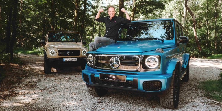 
				Matthias Malmedie sitzt seitlich auf der Motorhaube einer vollelektrischen G-Klasse EDITION ONE in MANUFAKTUR Lackierung Sdseeblau magno und hebt lchelnd beide Fuste hoch, links dahinter steht eine weitere vollelektrische G-Klasse in MANUFAKTUR Lackierung Wstensand uni.
				