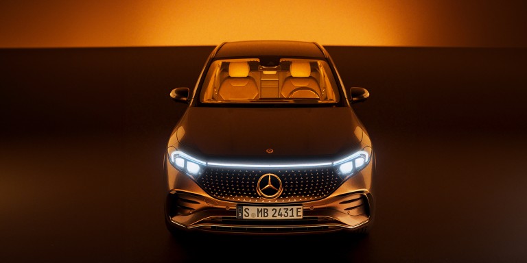 
				Frontalansicht eines EQS SUV vor einem abstrakten, orange-braunen Hintergrund.
				