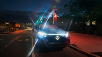 
Nahaufnahme eines Mercedes-Benz bei Nacht auf einer Strae. Seine Scheinwerfer berstrahlen das Bild, auch der Mercedes-Stern leuchtet.
