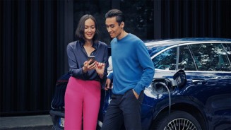 
Eine Frau und ein Mann stehen vor einem Mercedes-Benz Fahrzeug, dessen Batterie aufgeladen wird. Sie zeigt ihm etwas auf dem Smartphone.
