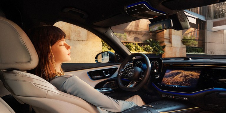 
				Eine Frau geniet hinterm Steuer eines Mercedes-Benz eine ENERGIZING COMFORT Sitzmassage.
				