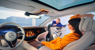 
						  Eine Frau sitzt auf dem Beifahrersitz eines EQS von Mercedes-Benz und blickt auf das Zentraldisplay, auf dem eine Kamin-Visualisierung zu sehen ist. An der geffneten Beifahrertr lehnt ein Mann.
						  