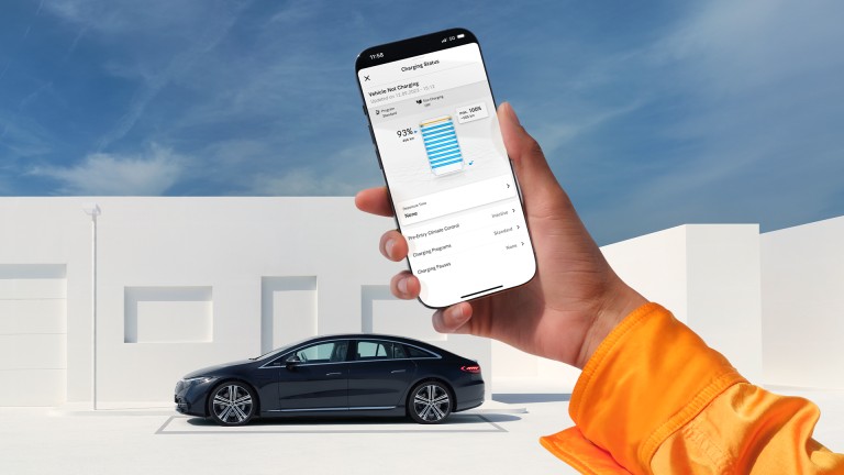 
			Eine Hand hlt ein Smartphone vor einem Mercedes EQS, der im Hintergrund parkt, auf dem Display ist die Mercedes me App geffnet, mit der der Ladestand des Fahrzeugs berprft wird. 
		