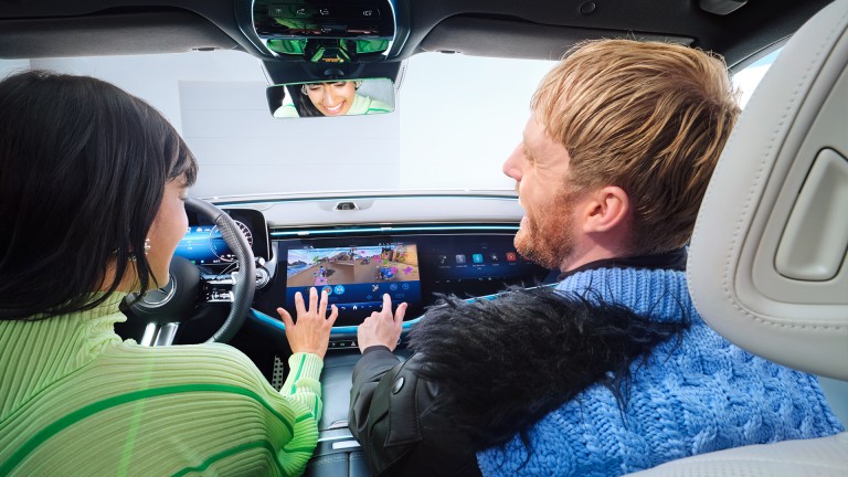 
			Blick von der Rckbank auf die vorderen Sitze eines EQS. Eine Frau sitzt auf dem Fahrersitz und spielt zusammen mit einem Mann auf dem Beifahrersitz am Zentraldisplay ber die In-Car-Apps ein Spiel.
		