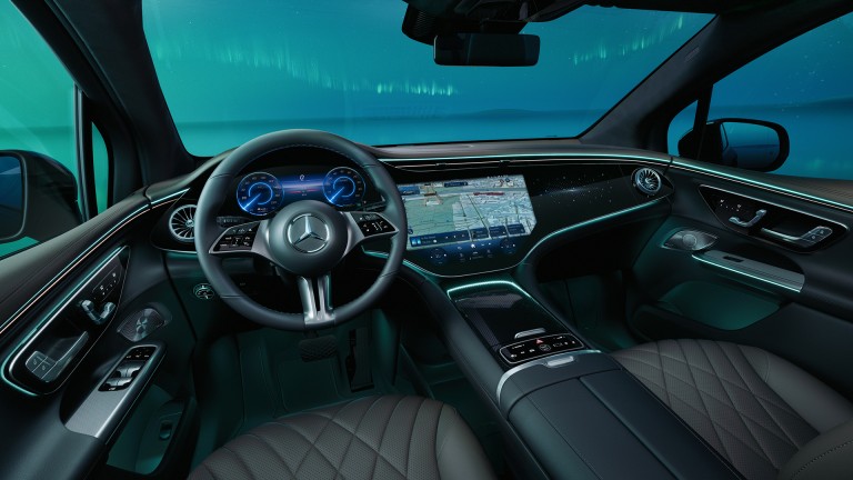 
			Blick vom Fahrersitz auf das Lenkrad, Beifahrer- und Zentraldisplay eines EQS SUV, durch die Windschutzscheibe sind grnliche Polarlichter zu sehen.
		