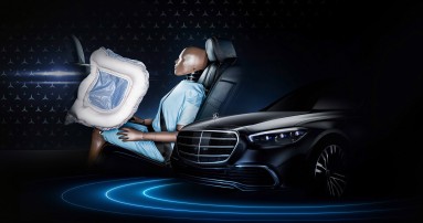 
						  Links ist ein Dummy in blauer Kleidung auf einem Fondsitz zu sehen, vor ihm ein entfalteter Frontalairbag, rechts daneben die Motorhaube eines schwarzen Mercedes-Benz Fahrzeugs mit Stern auf der Haube.
						  