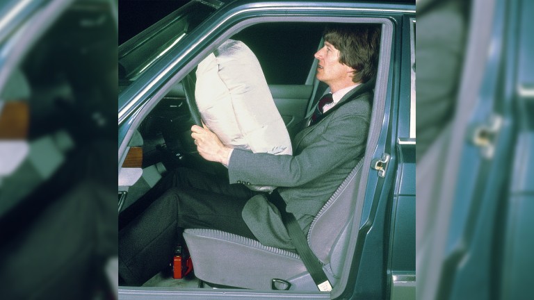 
			Ein Mann im Anzug sitzt angeschnallt am Steuer einer Mercedes-Benz S-Klasse, an deren Lenkrad sich der Fahrer-Airbag entfaltet.
		