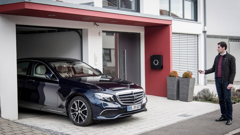 
			Eine Mercedes-Benz E-Klasse parkt in eine Garage, whrend der Fahrzeugbesitzer rechts danebensteht und den Vorgang ber sein Smartphone steuert.
		