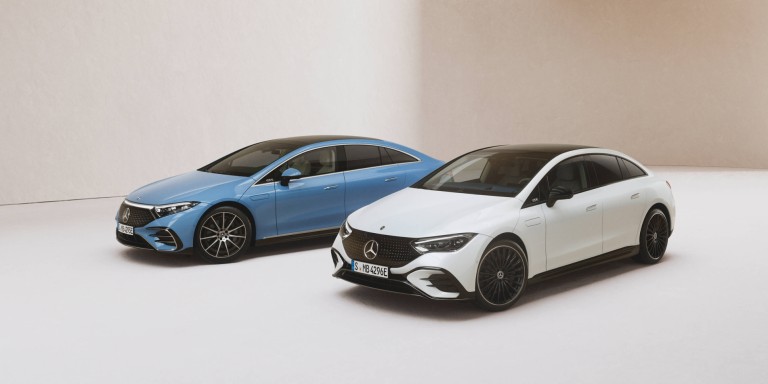 
				Zwei Mercedes-Benz Fahrzeuge stehen nebeneinander vor einem beigefarbenen Hintergrund, links ein EQS in MANUFAKTUR vintageblau uni, rechts daneben ein EQE in Polarwei.
				
