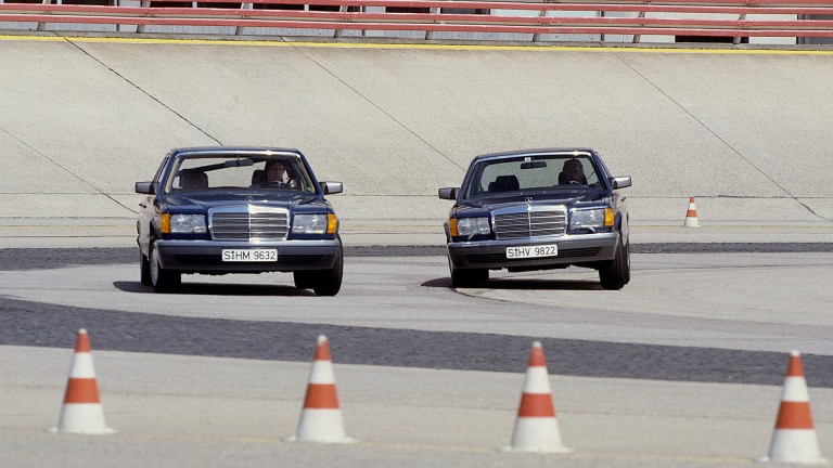 
			Zwei Mercedes-Benz S-Klassen der Baureihe 126 fahren auf einer Teststrecke, um das aktive Federungssystem ABC zu testen. Im Vordergrund am Rand der Fahrbahn sind vier Pylonen zu erkennen.
		