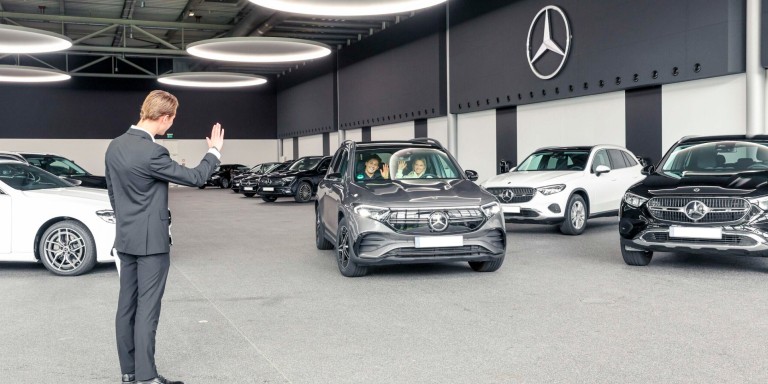 
				Kundendienstmitarbeiter Jonathan Vielhaber verabschiedet Mercedes-Benz Members Kundin Lena Celine Breimeier in ihrem neuen EQB.
				