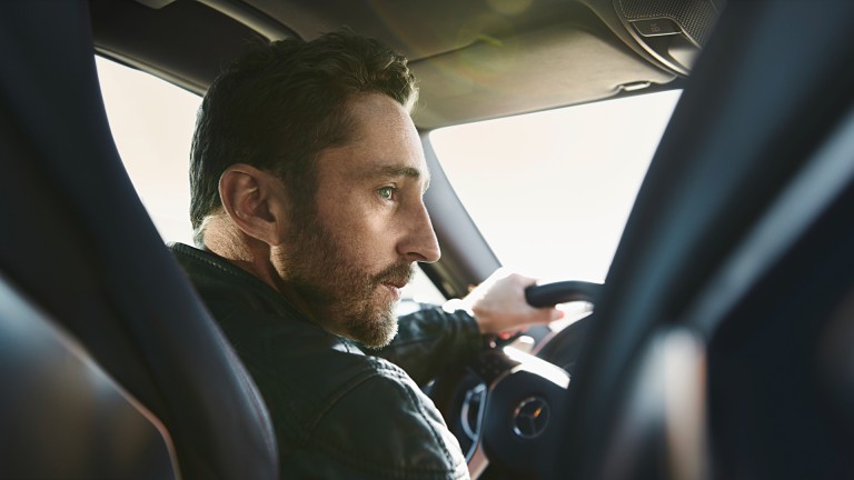 
			Ein Mann sitzt am Steuer eines Mercedes-Benz Fahrzeugs und hlt mit der linken Hand das Steuer fest, whrend er einen Blick nach rechts wirft.
		