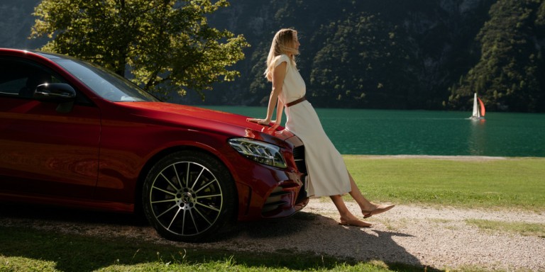 
				Eine Frau lehnt sich an einen Mercedes-Benz und geniet die Sonne.
				