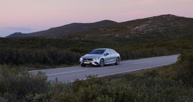 
						  Ein Mercedes-Benz fhrt ber eine Strae, umgeben von grner Landschaft.
						  