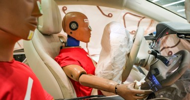 
						  Blick vom Beifahrersitz auf den Fahrersitz eines Mercedes-Benz Fahrzeugs, auf denen zwei Dummys in roten T-Shirts sitzen. Die Windowbags und der Fahrerairbag sind entfaltet.
						  