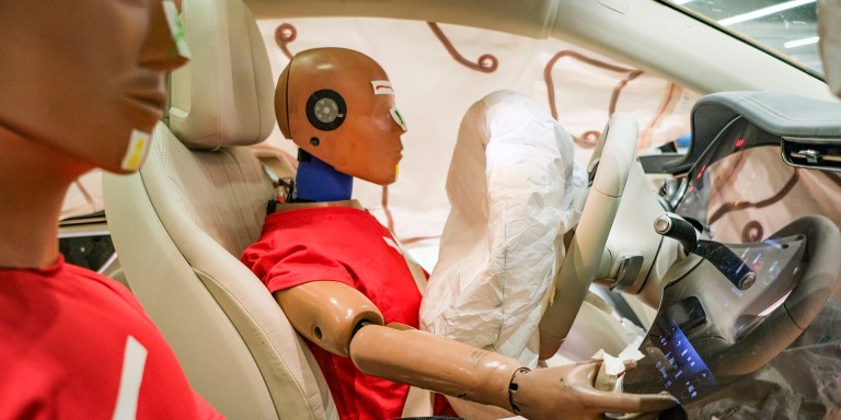 
				Blick vom Beifahrersitz auf den Fahrersitz eines Mercedes-Benz Fahrzeugs, auf denen zwei Dummys in roten T-Shirts sitzen. Die Windowbags und der Fahrerairbag sind entfaltet.
				