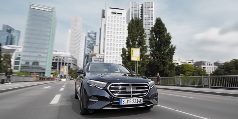 
				Eine E-Klasse Plug-in-Hybridmodell in nautikblau fhrt auf einer Strae, im Hintergrund ist Frankfurts Skyline zu sehen.
				