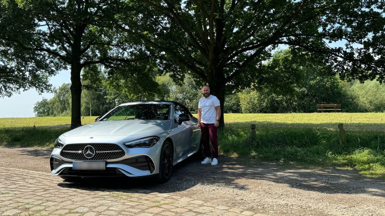 
			Aufnahme von vorne: Serhat Balak steht neben der Fahrertr seines Fahrzeugs.
		