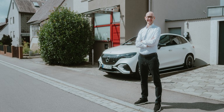 
				Mercedes-Benz Produkttrainer Christoph Geissler steht vor einem Einfamilienhaus und verschrnkt lchelnd die Arme. Hinter ihm parkt ein Mercedes-AMG EQE 43 SUV in MANUFAKTUR opalithwei bright.
				