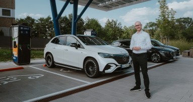 
						  Mercedes-Benz Produkttrainer Christoph Geissler steht an einer ffentlichen Ladesule vor einem Mercedes-AMG EQE 43 SUV in MANUFAKTUR opalithwei bright, dahinter parken zwei weitere Mercedes-Benz Fahrzeuge.
						  
