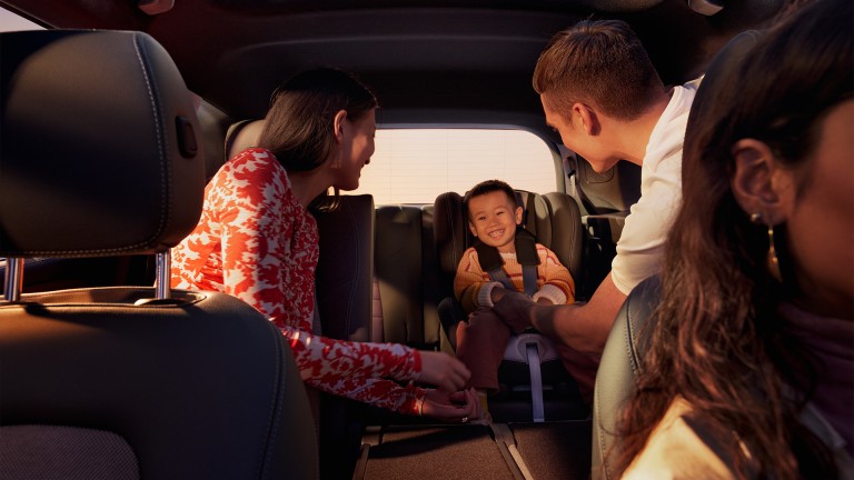 
			 Blick auf die hinteren Sitzreihen eines EQB von Mercedes-Benz, vorne rechts ist die Fahrerin zu sehen, dahinter sitzen eine Frau und ein Mann, die ein Kind ansehen, das lachend in der dritten optionalen Sitzreihe im Kindersitz sitzt.
		